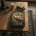 Book titled 'YAWT YAWT's Complete Guide to Hunting, Trappin' & Cookin' Critters' on a wooden table with a candle and books in the background.